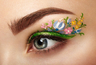 A woman’s hazel eye with green eye shadow and spring flowers as makeup art.