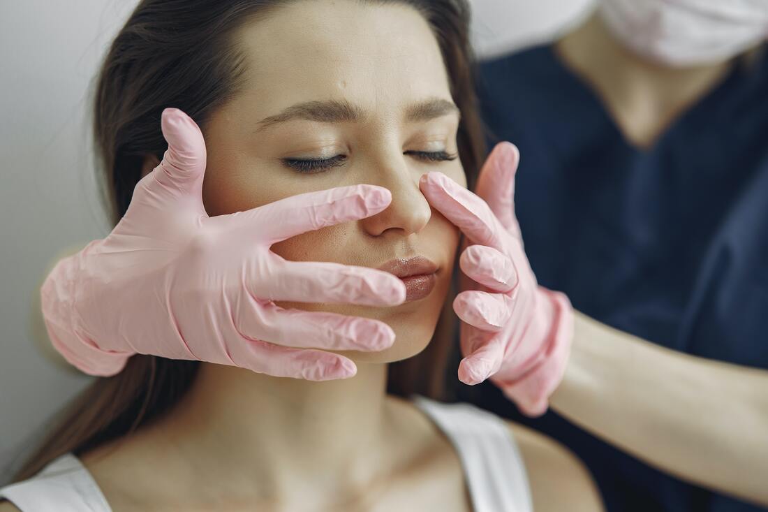 A beautician touching a woman’s face wearing gloves.