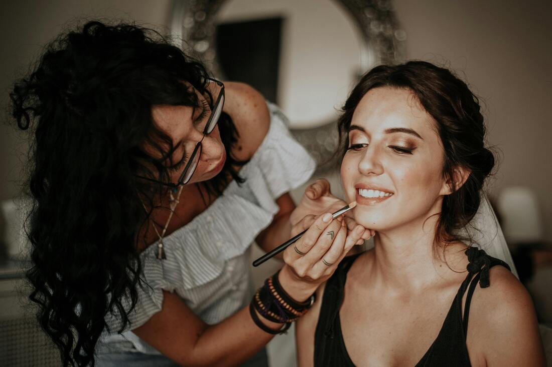 A woman applying lipstick on another woman who is sitting