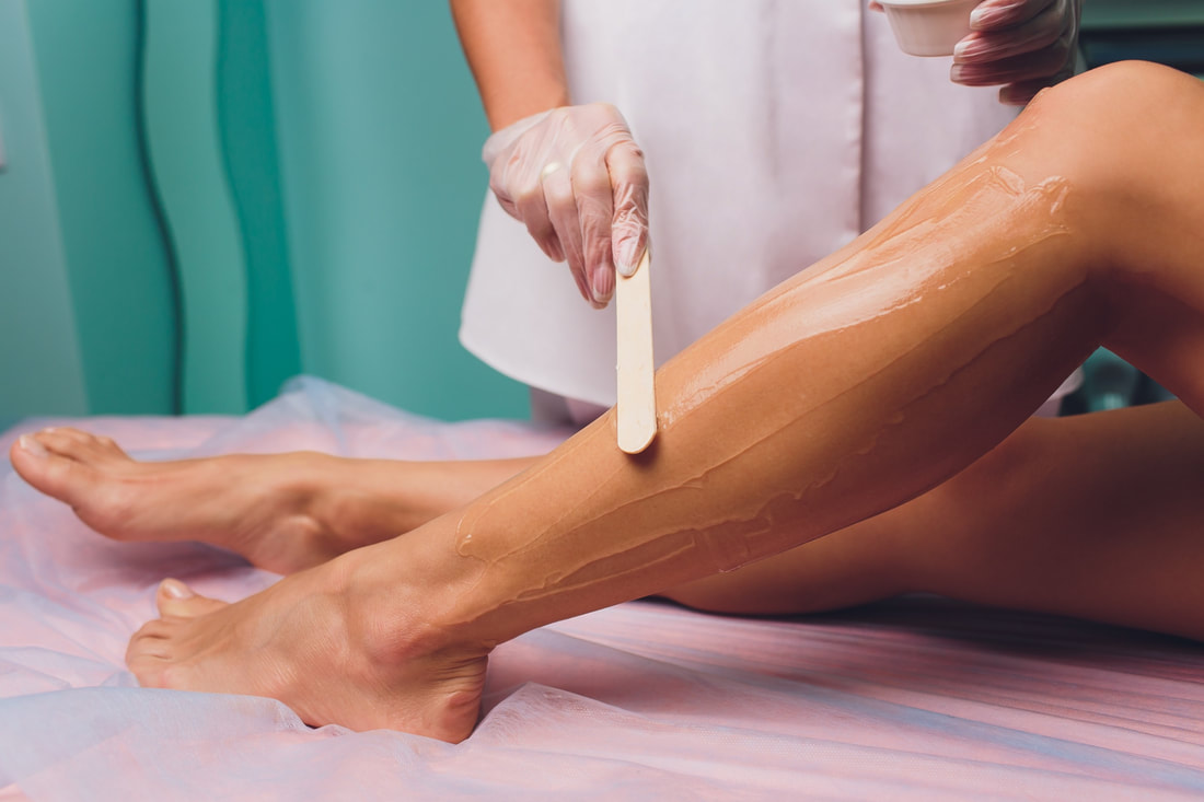 A beautician applies wax to a woman’s legs.