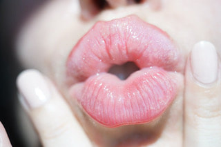 Female lips in a beautiful shimmery pink gloss with two fingers around her mouth.