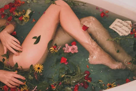 Person in bathtub with flowers in the water.